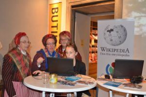 Staff member Sophie Österberg in a demonstration of Wikipedia for members of Sorunda ward association in traditional dresses on the day of the fifth anniversery of Wikimedia Sweden. "Hembygdens helg 2012 02" by Axel Pettersson, under CC-BY-SA 3.0 Unported, from Wikimedia Commons