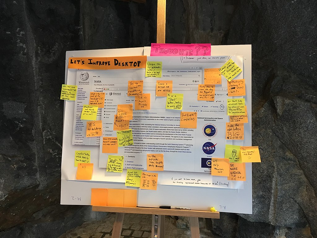 Sticky notes with messages of feedback on a large mockup poster for the Desktop improvements project