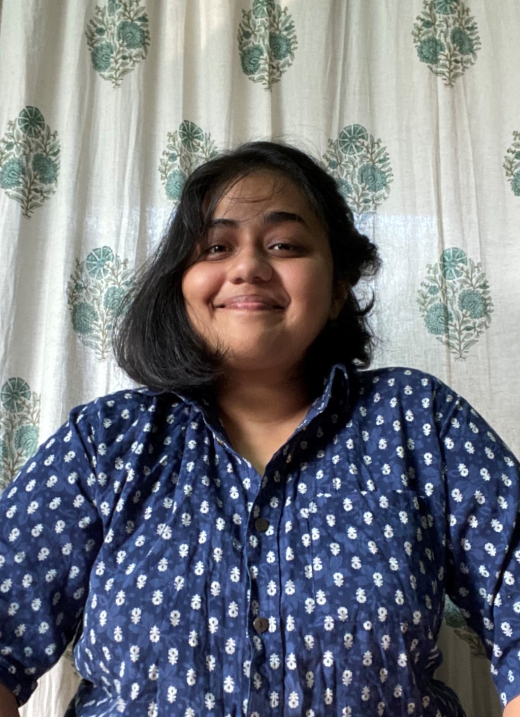 Photo of Aditi Abhijit Kulkarni smiling at the camera wearing a blue and white button down shirt.