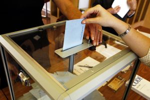 A picture of a person entering their ballot envelope into a ballot box.