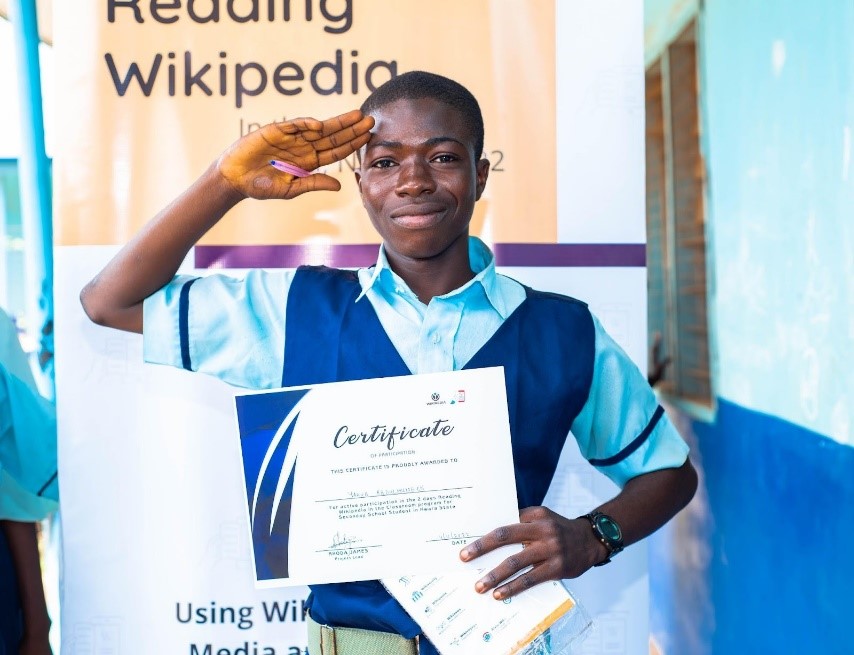 RWC Student salutes with his certificate and Student Guide held to his chest at GHS Adeta