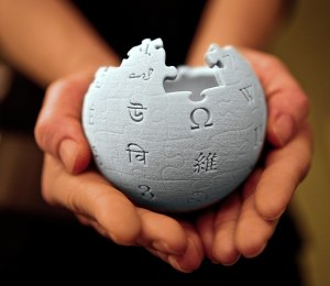 A three-dimensional model of the Wikipedia logo held in a person's hands.