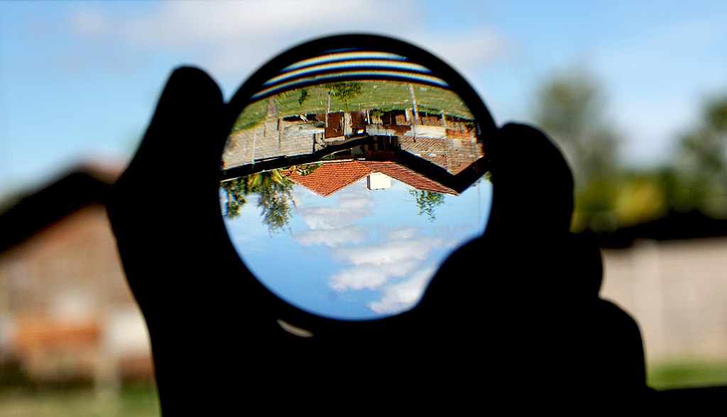 A view of buildings with clay roof tiles through a convex lens and a blue sky surrounding