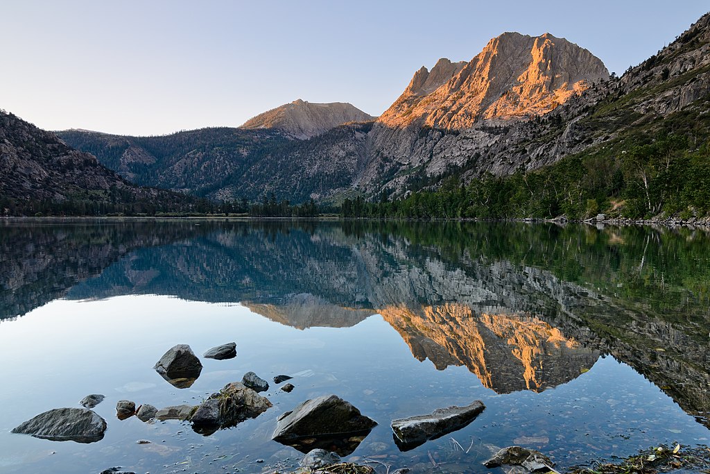 Silver Lake in California, a reflective lake surrounded by green trees and mountains with a reddish brown hue.