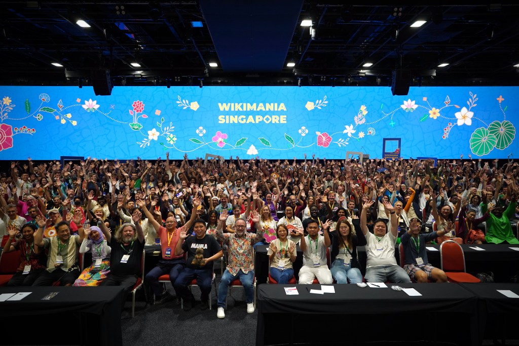 A photograph of 2023 Wikimania Singapore attendees raising their hands in celebration